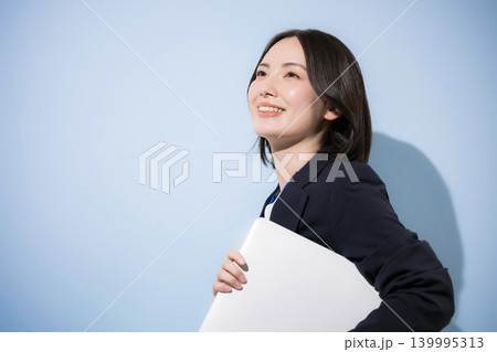 水色背景で名札をつけたノートパソコンを持つ働くかわいい女性社員のビジネスとITなどのイメージ見上げる 139995313