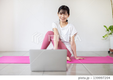 ノートパソコンを見ながらヨガの練習をする日本人の若い女性 139997204
