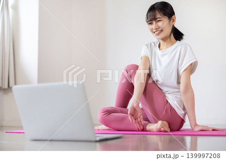 ノートパソコンを見ながらヨガの練習をする日本人の若い女性 ノートパソコンを見ながらヨガの練習をする日本人の若い女性 139997208