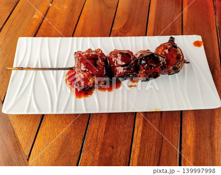 Grilled meatballs on skewers and served with sweet and spicy sauce on a white square plate with a wooden table background 139997998