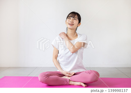 ヨガマットの上で肩をセルフマッサージする日本人の若い女性 139998137