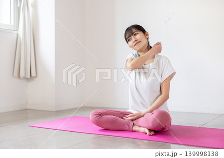 ヨガマットの上で肩をセルフマッサージする日本人の若い女性 139998138