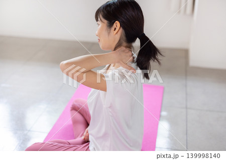 ヨガマットの上で肩をセルフマッサージする日本人の若い女性 139998140