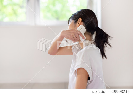 ヨガマットの上でマッサージガンで肩をセルフマッサージする日本人の若い女性 139998239