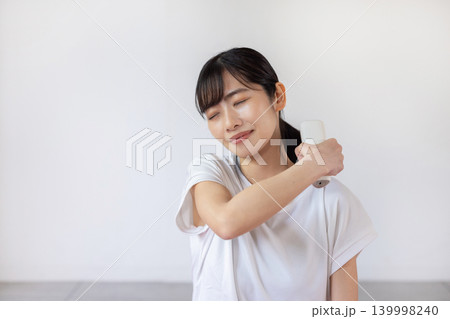 ヨガマットの上でマッサージガンで肩をセルフマッサージする日本人の若い女性 139998240