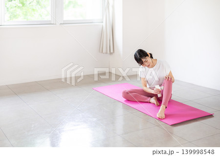 ヨガマットの上でマッサージガンで足をセルフマッサージする日本人の若い女性 139998548
