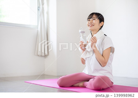 ヨガマットの上でウォーターボトルを手に微笑む日本人の若い女性 139998962