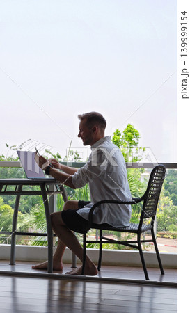 Man Using Smartphone Near Laptop At Hotel Balcony Workspace During Remote Work Routine, Digital Nomad Lifestyle And Mobile Productivity Concept 139999154