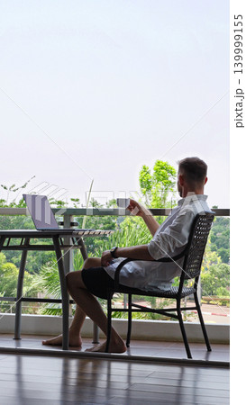 Man Drinking Coffee At Hotel Balcony Workspace During Remote Work Routine, Calm Digital Nomad Lifestyle And Flexible Work Life Balance Concept 139999155
