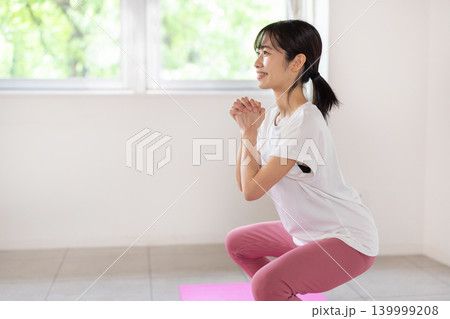 明るい室内で笑顔でスクワットをする日本人の若い女性 明るい室内で笑顔でスクワットをする日本人の若い女性 139999208