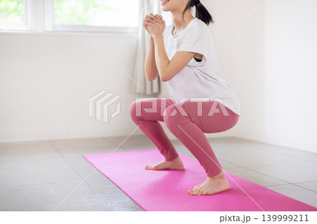 明るい室内で笑顔でスクワットをする日本人の若い女性 明るい室内で笑顔でスクワットをする日本人の若い女性 139999211