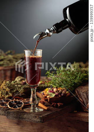 Herbal bitter liqueur is poured from a vintage bottle into a glass. Herbal bitter liqueur is poured from a vintage bottle into a glass. 139999357