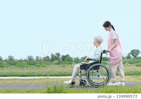土手を散歩する車椅子に乗った日本人シニア女性と若い日本人介護士の女性 土手を散歩する車椅子に乗った日本人シニア女性と若い日本人介護士の女性 139999572