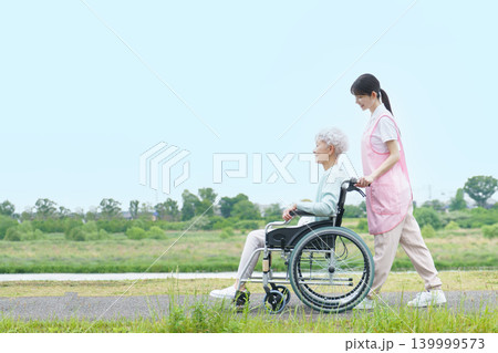 土手を散歩する車椅子に乗った日本人シニア女性と若い日本人介護士の女性 139999573
