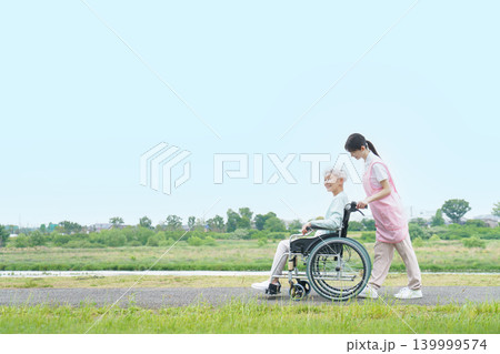 土手を散歩する車椅子に乗った日本人シニア女性と若い日本人介護士の女性 土手を散歩する車椅子に乗った日本人シニア女性と若い日本人介護士の女性 139999574