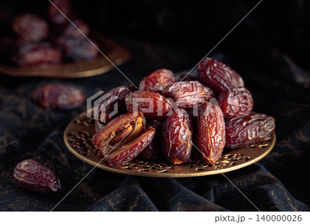 Dates fruits in a golden bowl on black fabric with gold ornamentation. Dates fruits in a golden bowl on black fabric with gold ornamentation. 140000026