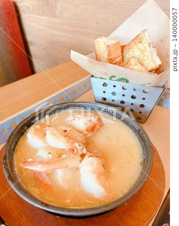 木目のテーブルに置かれたスキレットの海老料理とバゲット付きのシュリンプアヒージョのランチタイム風景 140000057
