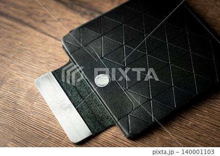 Handmade black wallet made of genuine leather on a wooden background. Close-up, top view. Handmade black wallet made of genuine leather on a wooden background. Close-up, top view. 140001103