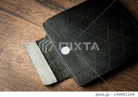 Handmade black wallet made of genuine leather on a wooden background. Close-up, top view. Handmade black wallet made of genuine leather on a wooden background. Close-up, top view. 140001104