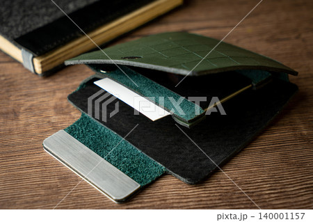 Handmade green wallet made of genuine leather on a wooden background. Close-up, top view. Handmade green wallet made of genuine leather on a wooden background. Close-up, top view. 140001157