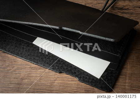 Handmade black wallet made of genuine leather on a wooden background. Close-up, top view. Handmade black wallet made of genuine leather on a wooden background. Close-up, top view. 140001175