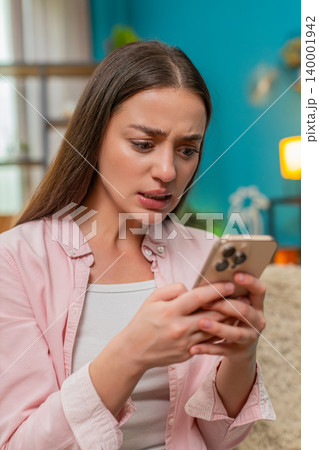 Young woman angrily texting on smartphone waving hand frustrated by chat messages and visible dismay Young woman angrily texting on smartphone waving hand frustrated by chat messages and visible dismay 140001942
