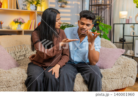 Indian couple man and woman sitting on home sofa arguing by smartphone during complaint call at home 140001960