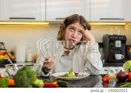 Young woman bored with healthy salad in kitchen at home during strict diet and weight loss struggle 140002051