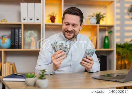 Young man on home table counting cash and planning budget savings and big expenses on laptop at home 140002054