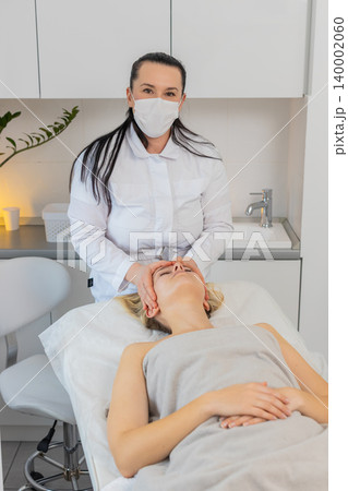Young woman receiving relaxing facial massage by professional beautician doctor in beauty clinic Young woman receiving relaxing facial massage by professional beautician doctor in beauty clinic 140002060
