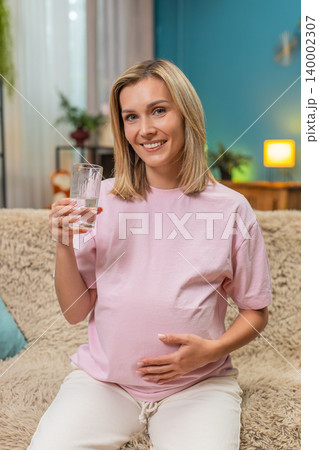 Pregnant woman drinking pure water hand on belly showing hydration importance for healthy pregnancy 140002307