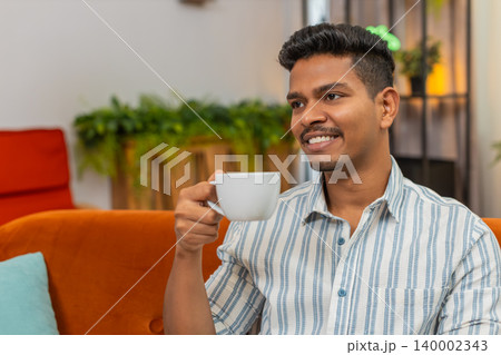 Indian man drinks coffee or tea warm cup relax recharge mood energy boost good morning start day joy Indian man drinks coffee or tea warm cup relax recharge mood energy boost good morning start day joy 140002343