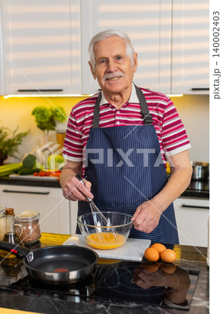 Senior old man whisking eggs for omelet in home kitchen healthy breakfast diet easy cooking routine Senior old man whisking eggs for omelet in home kitchen healthy breakfast diet easy cooking routine 140002403