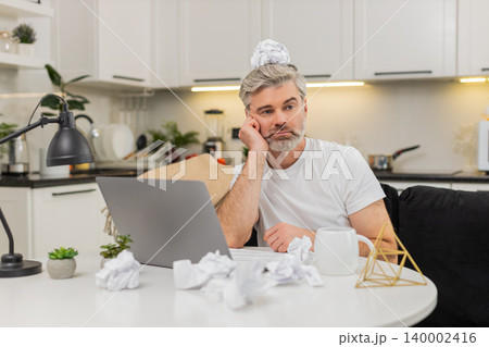 Middle-aged man drafts project notes at table burnout fatigue low motivation crumpled paper at home Middle-aged man drafts project notes at table burnout fatigue low motivation crumpled paper at home 140002416
