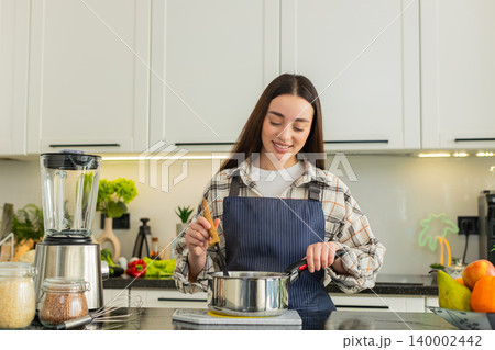 Young woman stirring hot vegetable soup in kitchen pot preparing healthy homemade lunch meal at home Young woman stirring hot vegetable soup in kitchen pot preparing healthy homemade lunch meal at home 140002442