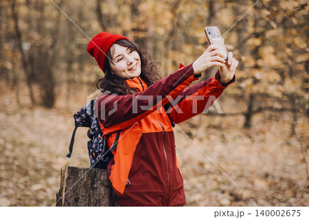 woman takes selfie or records video with smartphone while hiking in autumn forest. influencer lifestyle outdoors, recording vlog in nature, female content creator, social media storytelling. 140002675
