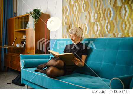 Reading a book while sitting on a turquoise couch in a modern living room during daylight hours 140003719