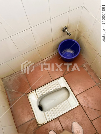 インドの建物内にあるバケツと蛇口が備え付けられた伝統的なスクワットタイプのトイレと床のタイル インドの建物内にあるバケツと蛇口が備え付けられた伝統的なスクワットタイプのトイレと床のタイル 140004891