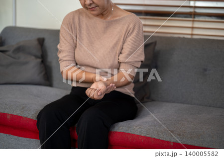 Elderly old asian woman grandma holding massaging a wrist getting pain ache while sitting on sofa. Elderly old asian woman grandma holding massaging a wrist getting pain ache while sitting on sofa. 140005582