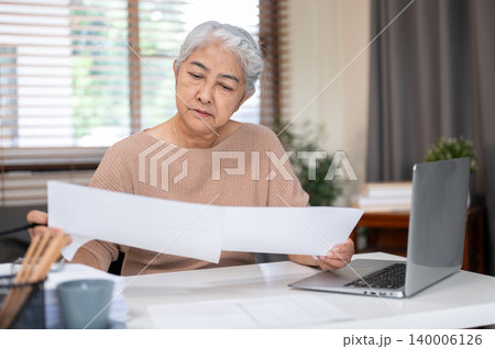 Senior old asian woman holding pencil looking reading paper document on working table at home office 140006126