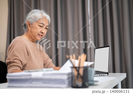 Grey hair senior old asian woman reading documents over laptop at working table at home or office 140006131