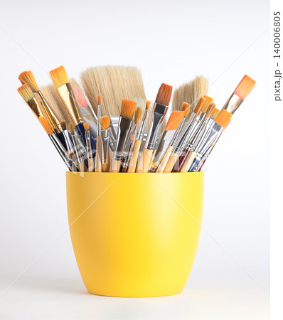 Artist paint brushes in a yellow flower pot. Mix of new and used artist brushes, in various sizes and widths, some made of synthetic hair and some of natural bristles. Front view over white. Photo Artist paint brushes in a yellow flower pot. Mix of new and used artist brushes, in various sizes and widths, some made of synthetic hair and some of natural bristles. Front view over white. Photo 140006805