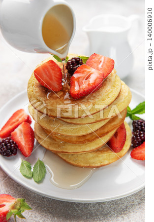 Pouring syrup over homemade pancakes with fresh berries 140006910