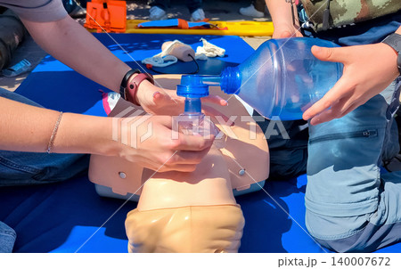 Children learning first aid during cpr training on a medical mannequin. Kids practicing artificial ventilation using an ambu bag resuscitator. 140007672