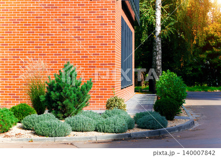 building brick wall corner shape yard floral garden landscape aesthetic space plant flower bed green bushes and decorative trees in summer ordinary morning sun rise lighting time street pavement 140007842