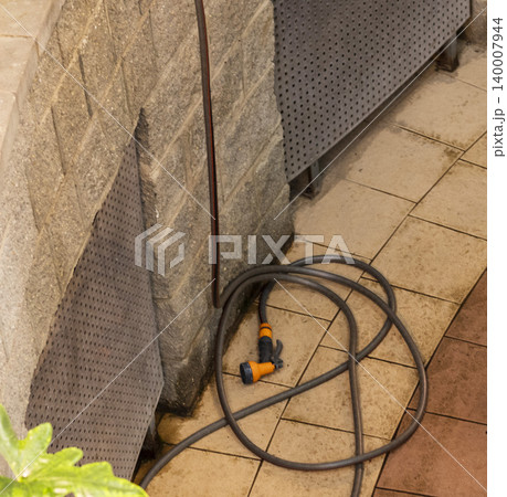 Coiled Garden Hose with Spray Nozzle on Atrium Tiled Floor. Household 140007944