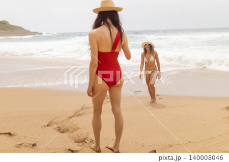 Women enjoying their time at the beach while walking on the sand near the ocean during a cloudy day Women enjoying their time at the beach while walking on the sand near the ocean during a cloudy day 140008046
