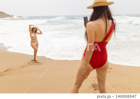 Women take photos on the beach while enjoying their time near the water under a cloudy sky Women take photos on the beach while enjoying their time near the water under a cloudy sky 140008047