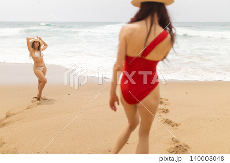 Friends enjoying time at the beach while walking on sand and playing near the waves in sunny weather 140008048