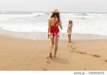 Two women walk along the beach leaving footprints in the sand on a sunny day by the ocean Two women walk along the beach leaving footprints in the sand on a sunny day by the ocean 140008058
